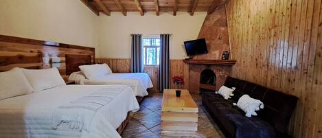 Una habitación con dos camas, un sofá, una chimenea, un televisor y piso de baldosas de piedra.