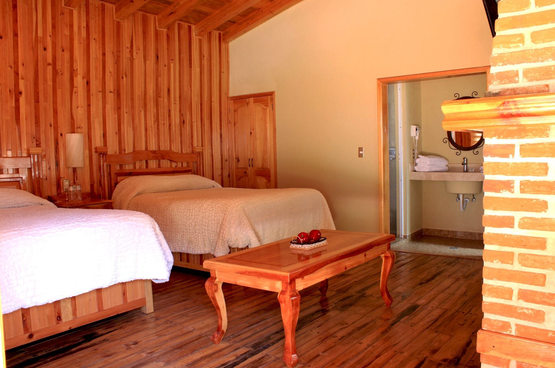 A wooden room with two beds, a wooden table, and a bathroom visible through an open door.
