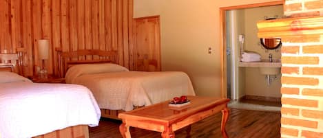 A wooden room with two beds, a wooden table, and a bathroom visible through an open door.