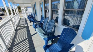 A covered outdoor seating area with blue Adirondack chairs and white railings. - Salty Snouts Retreat, Pet Friendly Home With Fire Pit in Holden Beach, NC (Holden Beach)
