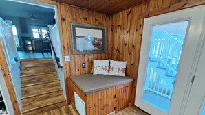 A wooden interior with a bench, a framed picture, and a view of a blue fence outside. - Salty Snouts Retreat, Pet Friendly Home With Fire Pit in Holden Beach, NC (Holden Beach)