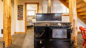 Eine rustikale Küche mit einem schwarzen Herd, Holzbalken und einem im Hintergrund sichtbaren Bett.