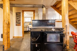 Cocina rústica con estufa negra, vigas de madera y una cama visible al fondo.