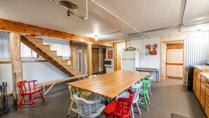 Eine geräumige Küche mit einem großen Holztisch, bunten Stühlen, einem Kühlschrank und einer Treppe, die in eine andere Ebene führt.