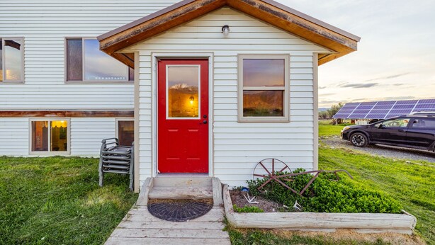 Ein Haus mit roter Tür, einer kleinen Veranda und Solaranlagen im Hintergrund.