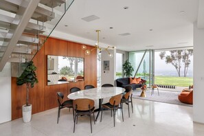 Een modern interieur met een eethoek, trap en grote ramen met uitzicht.