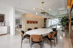 A modern dining area with a round marble table surrounded by chairs, a staircase, and a large potted plant. - Vue Modern (Beverly Hills)