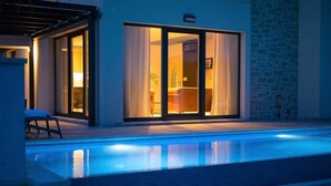 Una casa moderna con piscina, grandes puertas correderas de vidrio y un muro de piedra.