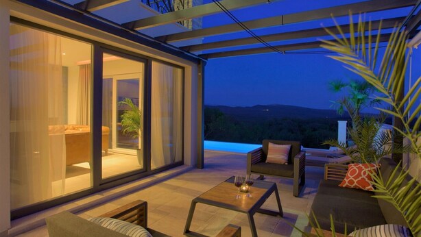 Un área exterior moderna con pared de vidrio, asientos cómodos y vistas al paisaje.