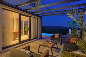 A modern outdoor living area with a glass wall, comfortable seating, and a view of the landscape. - Villa Wisteria with Pool (Vrbnik)