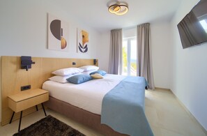 A modern bedroom with a large bed, a bedside table, a TV, and artwork on the wall. - Villa Wisteria with Pool (Vrbnik)
