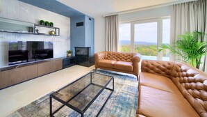Una sala de estar moderna con un sofá de cuero, un televisor de pantalla plana, una chimenea y un ventanal con vistas panorámicas.