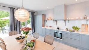 Una cocina moderna con gabinetes grises, un horno de acero inoxidable y un comedor con sillas de mimbre y una mesa de madera.