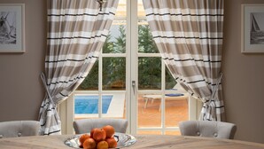 Comedor con mesa dispuesta para cuatro, un cuenco de naranjas y vista a un área de piscina exterior a través de una puerta de cristal.