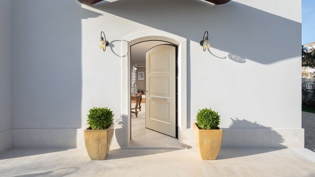 Una entrada moderna con una puerta blanca, dos luces empotradas en la pared y dos plantas en macetas.