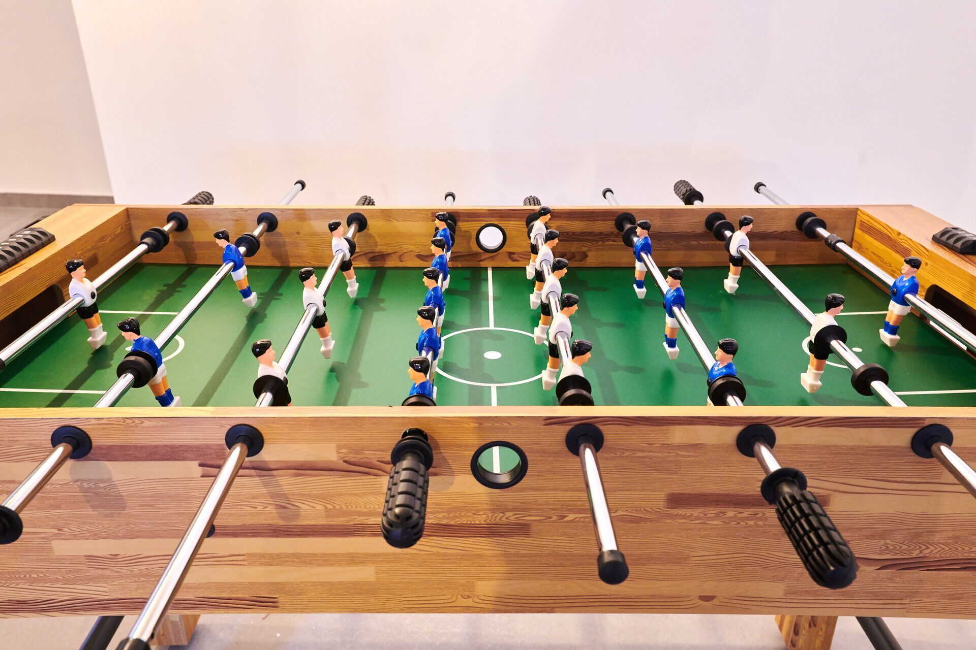 Ett fotbollsspel i trä med två lag, ett i blått och ett i vitt, placerat på en grön spelplan med ett centralt målområde.
