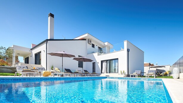 Ein modernes Haus mit Pool, Sitzgelegenheit im Freien und blauem Himmel.