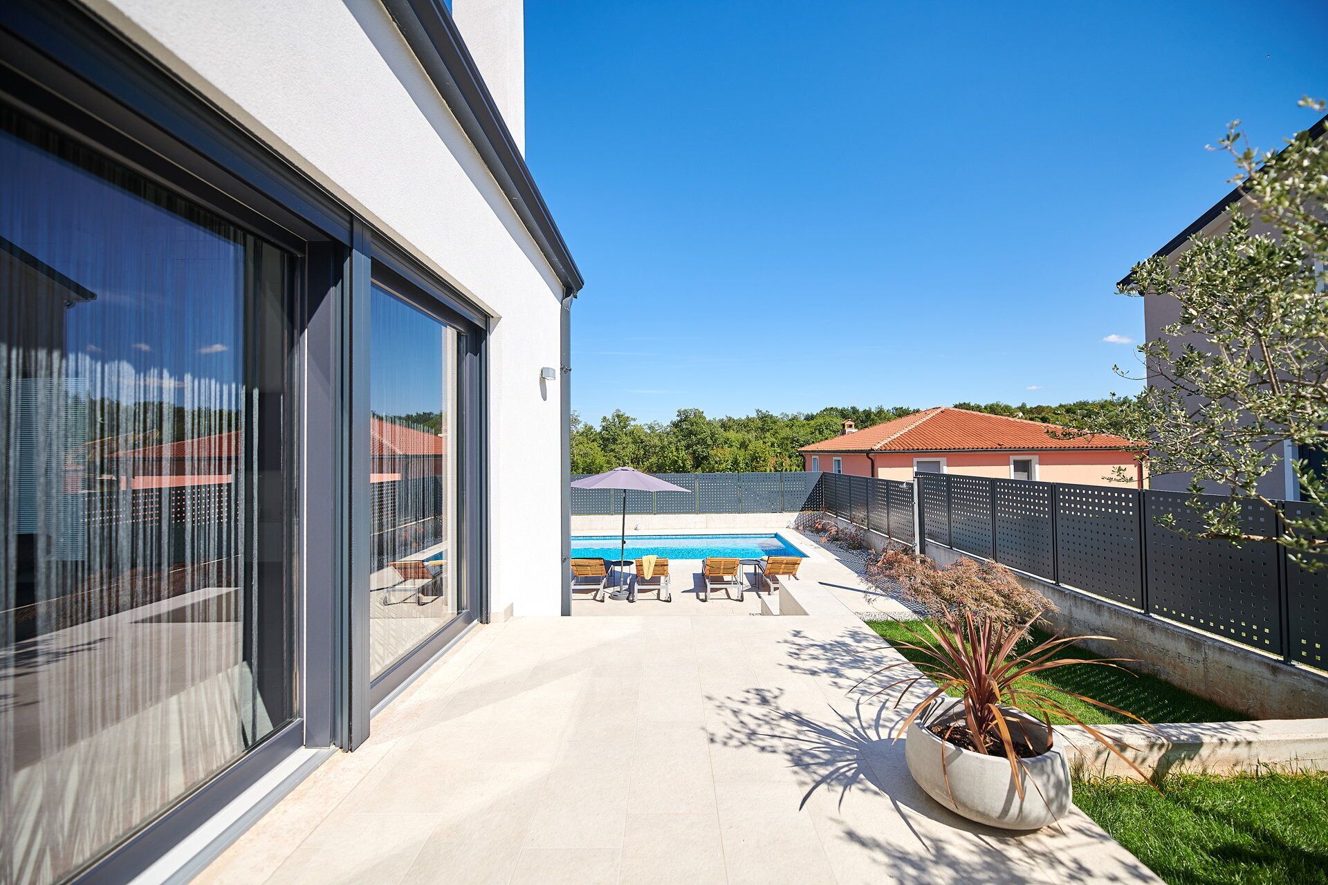 A modern house with a large glass door, a swimming pool, and a patio area with outdoor furniture.