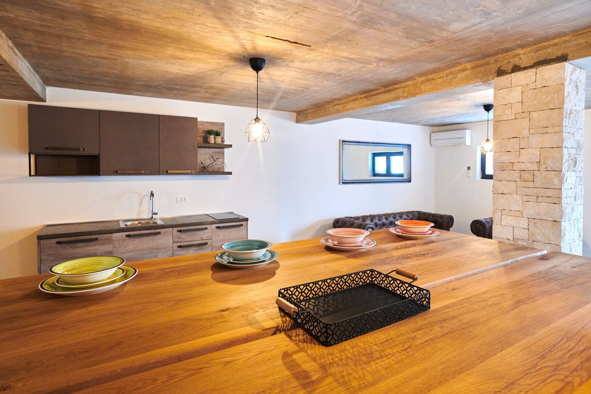 A modern kitchen with wooden cabinets, a large wooden dining table, and a stone accent wall.