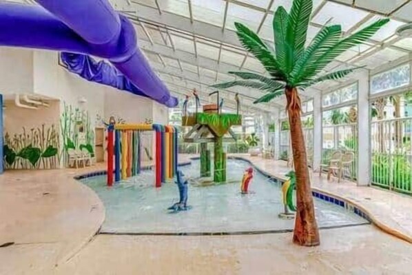 Parque acuático interior con toboganes, piscina y una palmera.