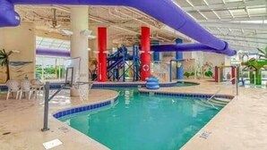 An indoor swimming pool with a slide, surrounded by pillars and a covered area. - Oceanfront Studio • Indoor Waterparks • Dunes Village Resort (Myrtle Beach)