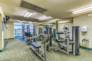 A gym with various exercise machines, a bench, and a large window offering a city view.