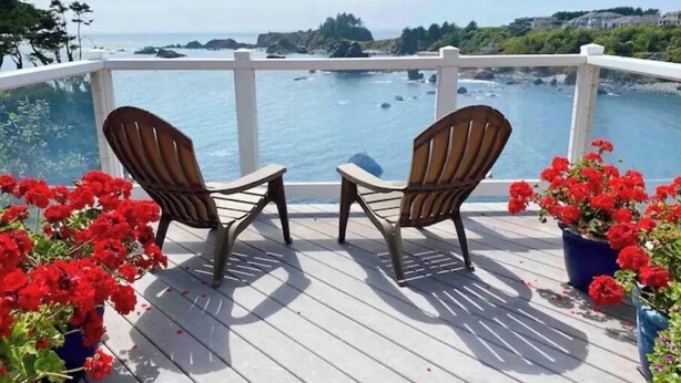 A wooden deck with two Adirondack chairs facing a scenic ocean view. - OCTOPUS SUITE, fire pit, BBQ, wildlife viewing platform, shared oceanfront deck. (Brookings)