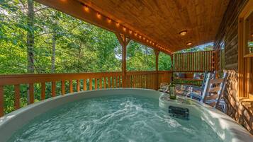 Un bain à remous doté d’une terrasse en bois et de rampes, entouré d’une végétation luxuriante.