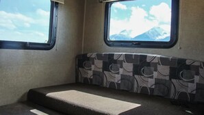 Interior de una caravana compacta con un banco acolchado, dos ventanas con vistas a las montañas y un escalón pequeño que lleva a la zona de la cama.