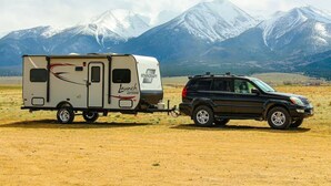Un tráiler de Starcraft enganchado a un SUV negro en un campo, con montañas nevadas al fondo.