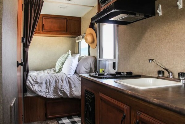 Compact kitchenette with sink, countertop, and utensils, adjacent to a cozy sleeping area.