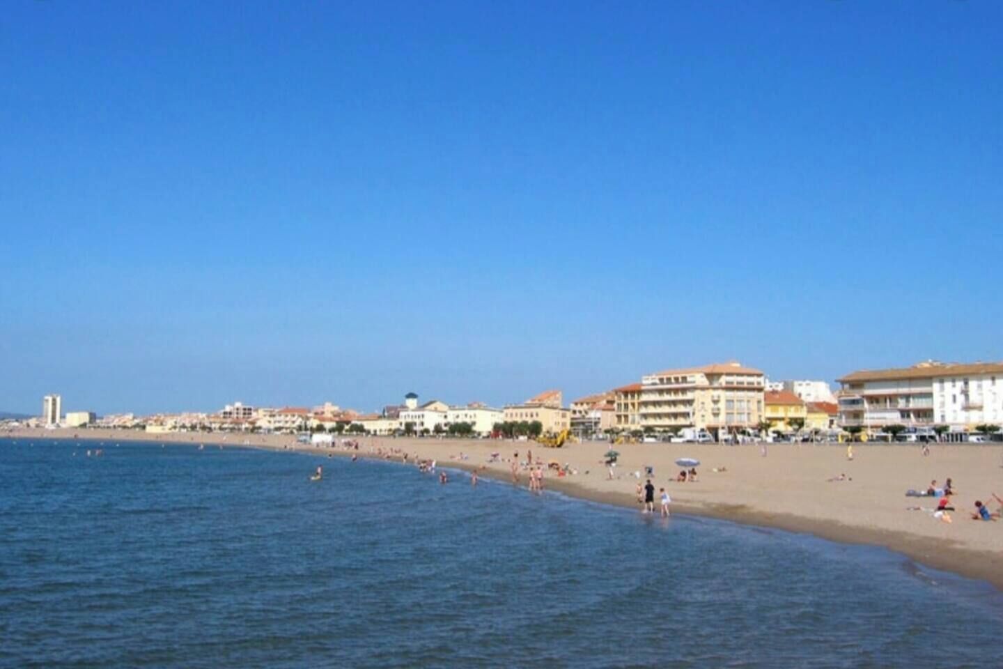 A beach with buildings along the shore, clear skies, and people enjoying the water.