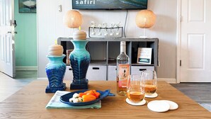 Ein Zimmer mit einem Holztisch, gedeckt mit einer Flasche Duplin Orange, zwei Gläsern Orangensaft, einem Teller mit Mozzarella und Tomaten sowie zwei dekorativen Vasen. An der Wand ist ein Fernseher angebracht, der eine Anzeige für eine Safari-Ferienhausvermietung zeigt.
