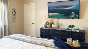 Ein Schlafzimmer mit einem Bett, einem Fernseher, der einen schönen Meerblick zeigt, einer Kommode und zwei Tassen Kaffee auf einem Tablett.