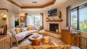 A modern living room with a fireplace, a sofa, a coffee table, and a view of the outdoors. - Luxury Joshua Tree Retreat w/ Hot Tub, BBQ and Games (Joshua Tree)