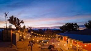 A backyard with a barbecue area, picnic table, and string lights. - Luxury Joshua Tree Retreat w/ Hot Tub, BBQ and Games (Joshua Tree)