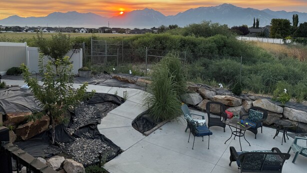 Un patio con mobiliario exterior, un sendero y vistas a las montañas al atardecer.