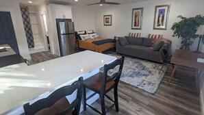 Una sala de estar moderna con un sofá, una mesa de comedor con sillas, un refrigerador y un ventilador de techo.