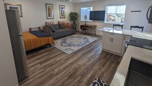 Un espacio habitable compacto con sofá, un escritorio pequeño, televisor y kitchenette.