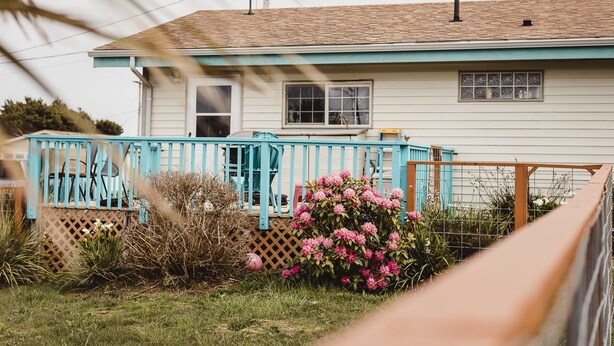 Ein Haus mit blauer Veranda und einem Garten mit rosa Blumen.
