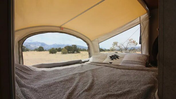 Ein Zelt mit einem Bett im Inneren, Blick auf eine Wüstenlandschaft und Berge in der Ferne.
