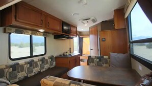 Ein kompaktes Wohnmobil-Interieur mit Küchenzeile, Essbereich und Sitzecke mit Blick ins Freie.