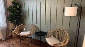 Een kamer met twee rieten stoelen, een klein rond tafeltje en een vloerlamp.