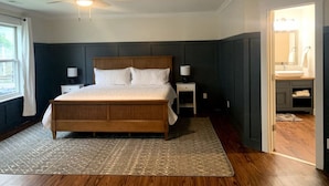 Een slaapkamer met een houten bed, een plafondventilator, een nachtkastje en een badkamer die door een open deur zichtbaar is.