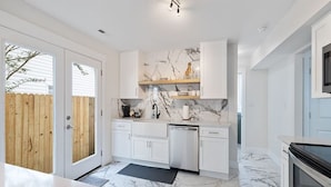 Een moderne keuken met witte kasten, marmeren vloeren en een inbouwoven.