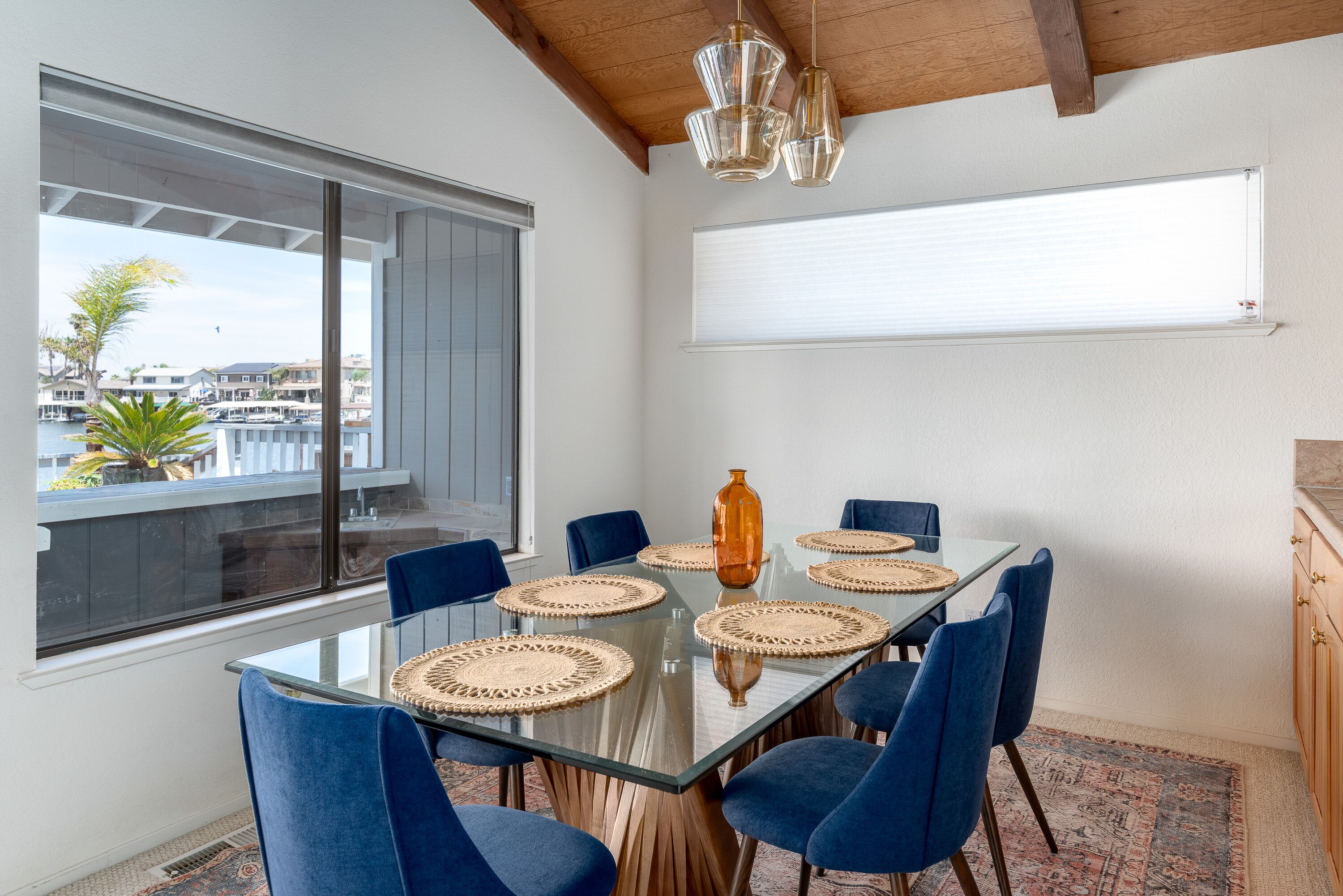 Un área de comedor moderna con una mesa de vidrio, sillas azules y vista al puerto deportivo.
