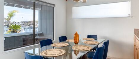Un área de comedor moderna con una mesa de vidrio, sillas azules y vista al puerto deportivo.