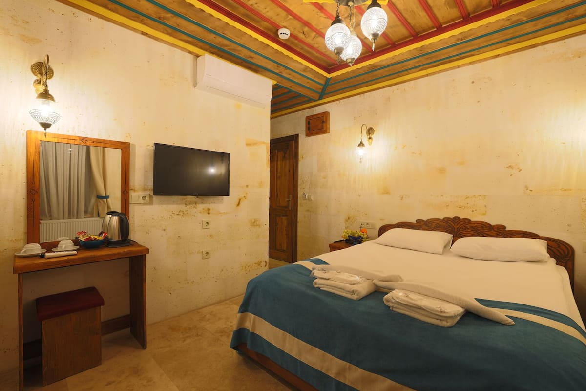 Habitación de hotel con cama, escritorio con espejo, televisión y techo con vigas de colores.