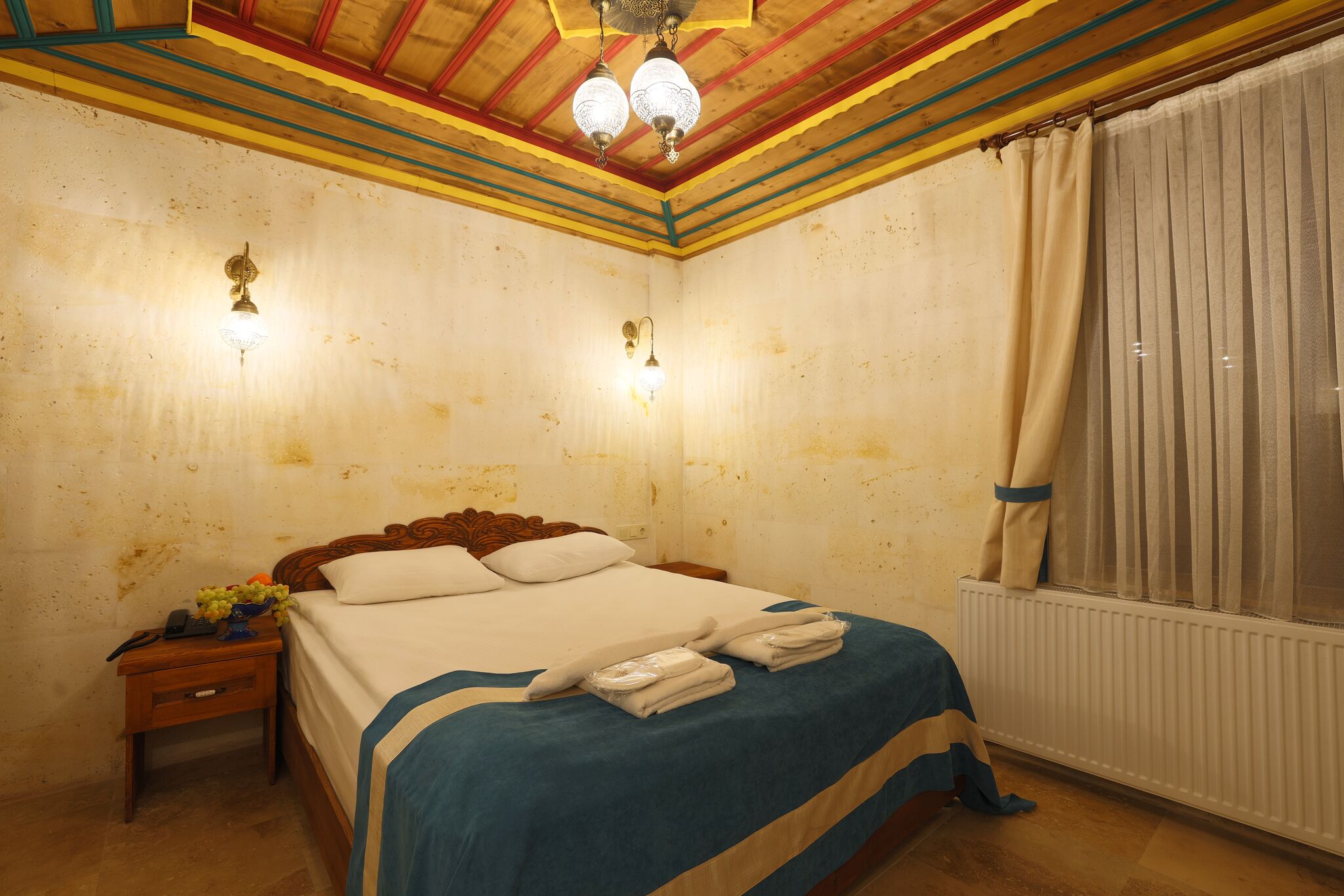 A hotel room with a wooden bed, bedside lamps, a nightstand, and a window with curtains.