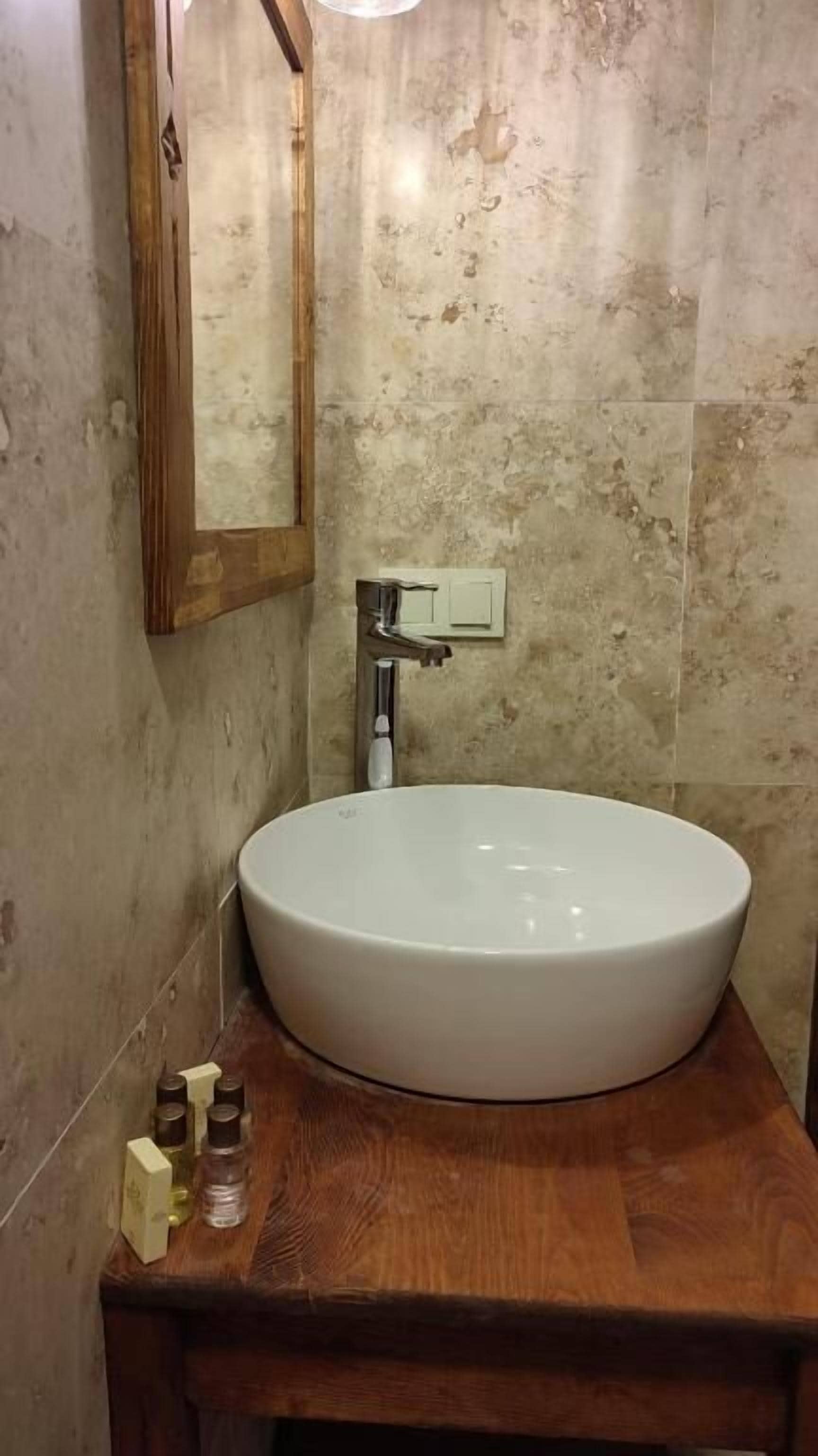 Un baño con un lavabo blanco redondo, encimera de madera y un espejo encima.